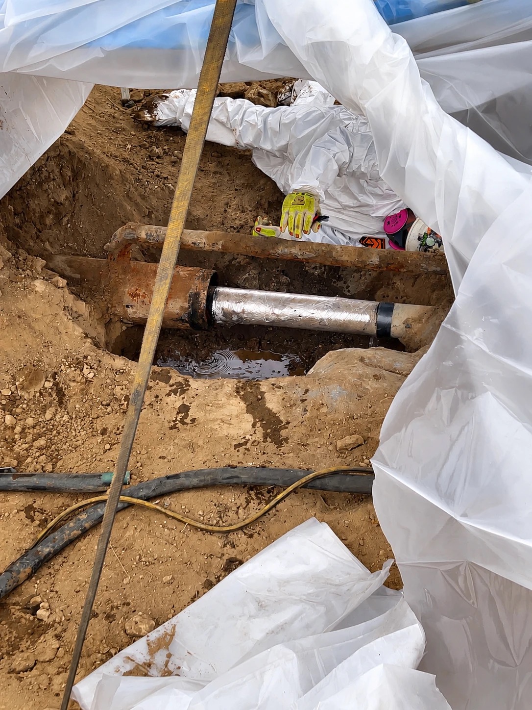 Exposed pipeline casing coupling under repair, wrapped and sealed, with water pooled in the excavated trench
